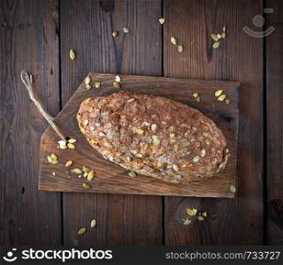 baked oval bread made from rye flour with pumpkin seeds on a wooden cutting board , top view