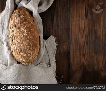 baked oval bread made from rye flour with pumpkin seeds on a gray linen napkin, top view, copy space