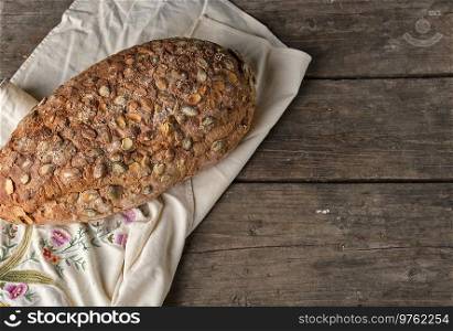 baked oval bread made from rye flour with pumpkin seeds on a gray linen napkin, top view, copy space