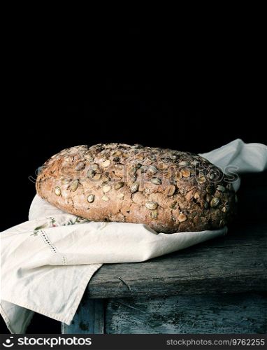 baked oval bread made from rye flour with pumpkin seeds on a gray linen napkin, black paper background 