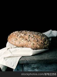 baked oval bread made from rye flour with pumpkin seeds on a gray linen napkin, black paper background 