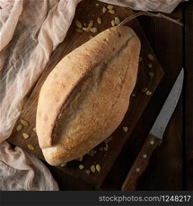 baked oval rye bread on a wooden cutting board, near the knife, top view, copy space