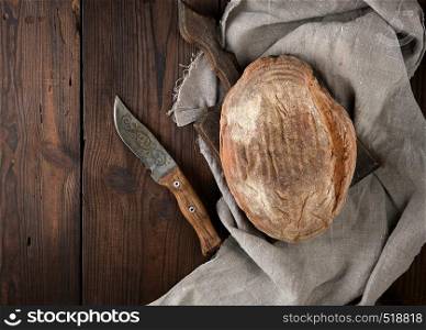 baked oval rye bread on a wooden cutting board, near the knife, top view, copy space