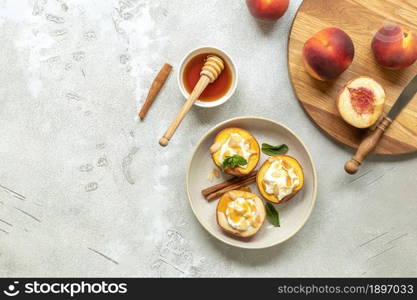 Baked peaches with cinnamon, almond petals, cream cheese, and honey on a light concrete background. Fruits in a plate with mint