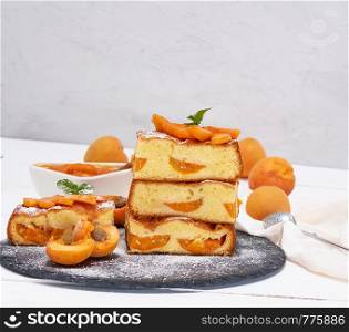baked pieces of biscuit pie with apricots on a black graphite plate, sponge cake