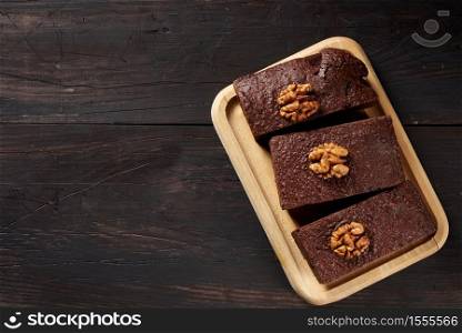 baked pieces of brownie chocolate cake with nuts on a rectangular wooden board, top view, place for inscription