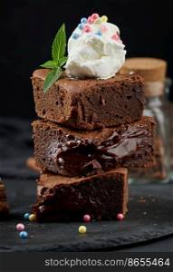 Baked pieces of chocolate brownie pie on a black table, on top of a scoop of ice cream
