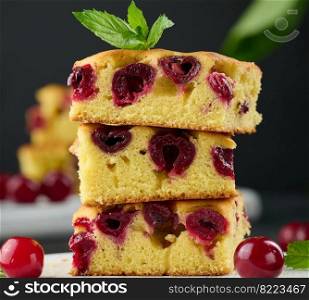 Baked pieces of sponge cake with red ripe cherries on a white wooden board