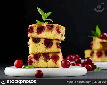 Baked pieces of sponge cake with red ripe cherries on a white wooden board