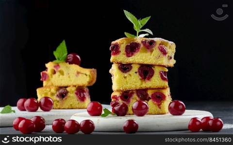 Baked pieces of sponge cake with red ripe cherries on a white wooden board