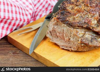 Baked pork meat with spices sliced on a cutting board with knife and fork.. baked pork meat