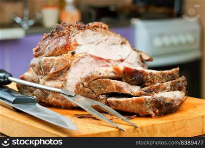 Baked pork meat with spices sliced on brown cutting board with knife and fork.. Baked pork meat with spices on brown wooden cutting board
