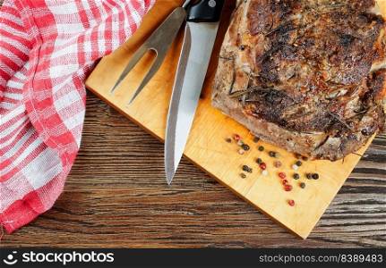 Baked pork meat with spices sliced on brown cutting board with knife and fork. Grilled meat. Top view, flat lay, copy space. Baked pork meat with spices on brown wooden cutting board