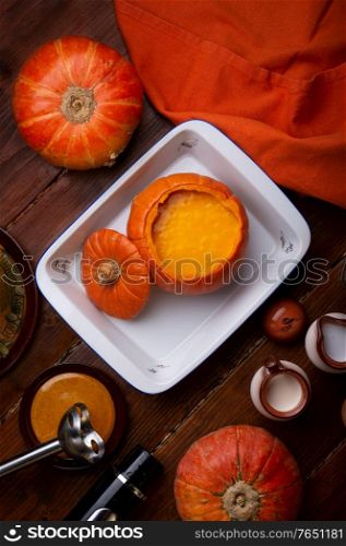 baked pumpkin cream coup served in pumpkin. served at wooden brown table with ripe orange pumkins. flat lay. healthy life concept