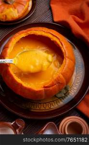 baked pumpkin cream coup served in pumpkin with corn. served at wooden brown table with ripe orange pumkins. flat lay. healthy life concept