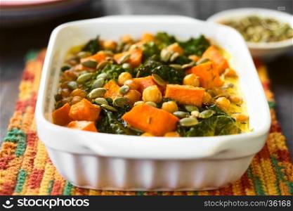 Baked pumpkin, kale and chickpea casserole with pumpkin seeds on top in casserole dish, photographed with natural light (Selective Focus, Focus one third into the dish)