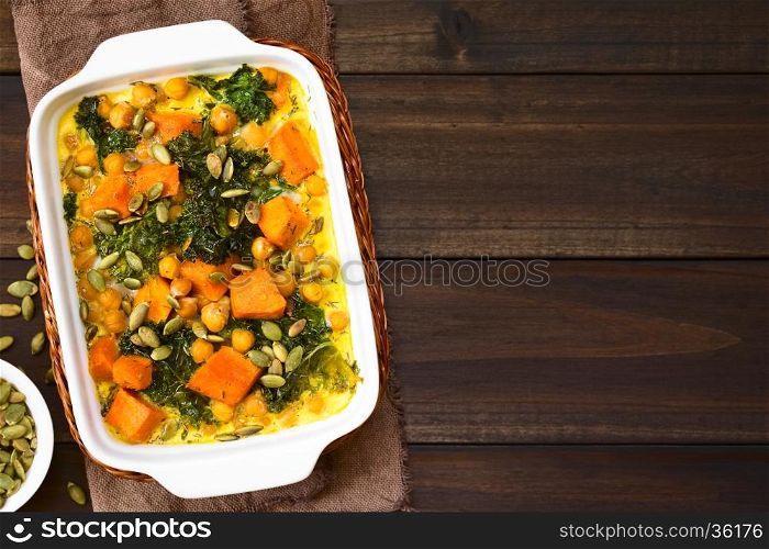 Baked pumpkin, kale and chickpea casserole with pumpkin seeds on top in casserole dish, photographed with natural light (Selective Focus, Focus on the top of the casserole)
