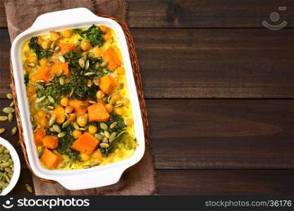 Baked pumpkin, kale and chickpea casserole with pumpkin seeds on top in casserole dish, photographed with natural light (Selective Focus, Focus on the top of the casserole)