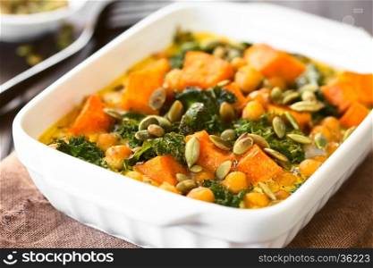 Baked pumpkin, kale and chickpea casserole with pumpkin seeds on top in casserole dish, photographed with natural light (Selective Focus, Focus one third into the image)