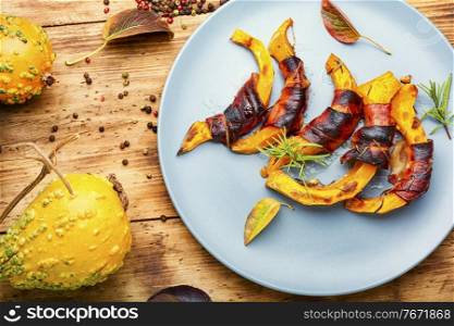 Baked pumpkin slices wrapped in bacon on rustic wooden table. Pumpkin slices wrapped in bacon