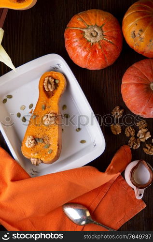 baked pumpkin with walnuts and seeds, coconut milk served at wooden brown table with ripe orange pumkins. flat lay. healthy life concept