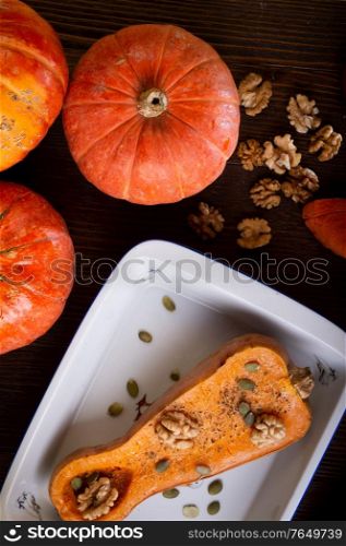 baked pumpkin with walnuts and seeds, coconut milk served at wooden brown table with ripe orange pumkins. flat lay. healthy life concept