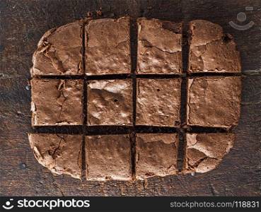 baked rectangular chocolate brownie pie is cut into squares, a wooden brown table