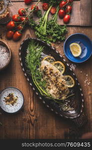 Baked roasted fish fillet in fish baking form with dill and lemon slices on wooden background, top view. Home cuisine concept. Seafood, low carb and dieting nutrition