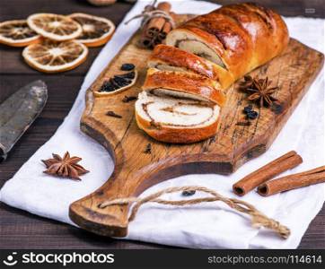 baked roll with cinnamon and nuts on a brown wooden board, close up