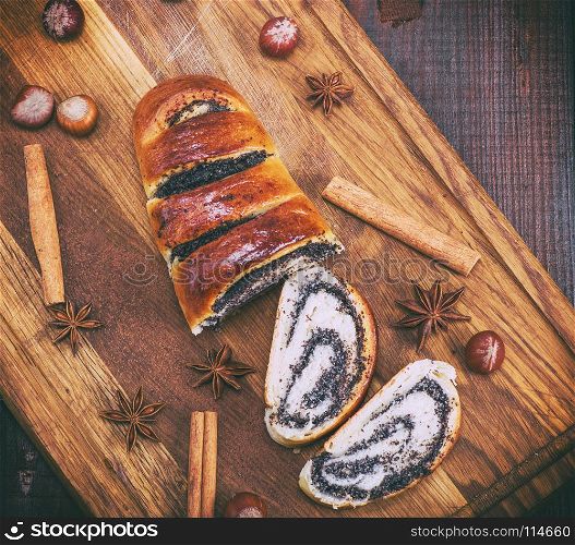 baked roll with poppy seeds on a wooden board, top view