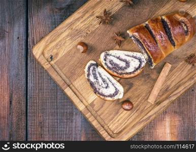 baked roll with poppy seeds on a wooden board, top view, empty space on the left