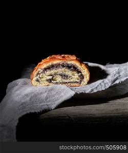 baked roll with poppy seeds on gray linen napkin, dark background