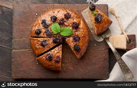baked round biscuit cake with nuts and berries topped, wooden brown table, top view, sponge cake