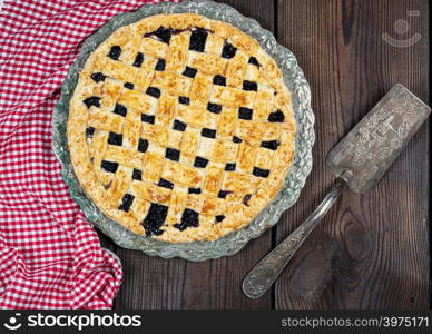 baked round black currant cake on an iron plate, top view, wooden brown background