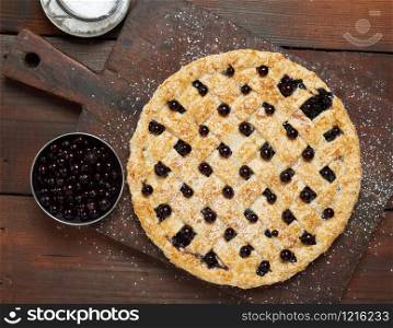 baked round black currant pie on wooden background, top view