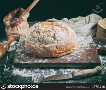 baked round bread, white wheat flour, old cutting board on a black table