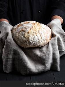 baked round homemade bread on a gray napkin, male hands show