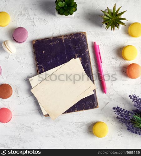 baked round macarons, empty postcards, notebook, pink pen and plants in a pot on a white background, top view