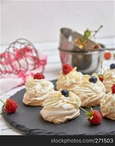 baked round meringues with whipped cream on a black graphite board, close up