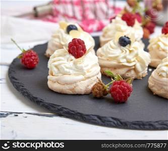 baked round meringues with whipped cream on a black graphite board, close up