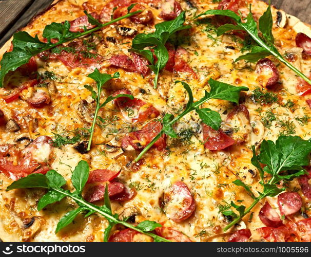 baked round pizza with smoked sausages, mushrooms, tomatoes, cheese and arugula leaves, food is cut in portions, full frame