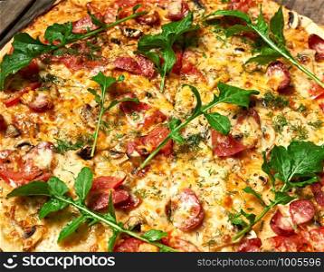 baked round pizza with smoked sausages, mushrooms, tomatoes, cheese and arugula leaves, food is cut in portions, full frame