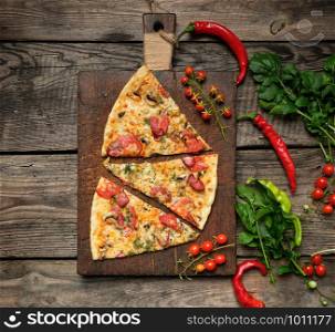 baked round pizza with smoked sausages, mushrooms, tomatoes, cheese and dill, sliced food on a brown wooden board, close up