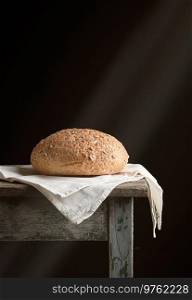 baked round rye bread lies on a gray linen napkin, black background,  sun’s rays from the window illuminate the bun