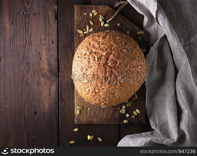baked round rye bread with sunflower seeds on a gray textile napkin, wooden background, top view