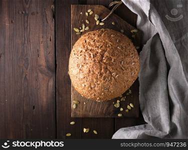 baked round rye bread with sunflower seeds on a gray textile napkin, wooden background, top view