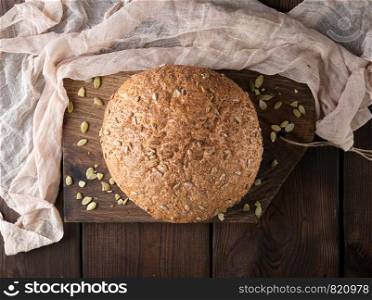 baked round rye bread with sunflower seeds on a textile napkin, wooden background, top view