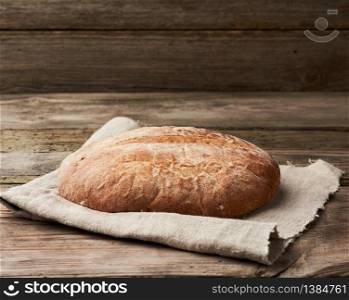 baked round rye flour bread on a kitchen gray napkin, top view
