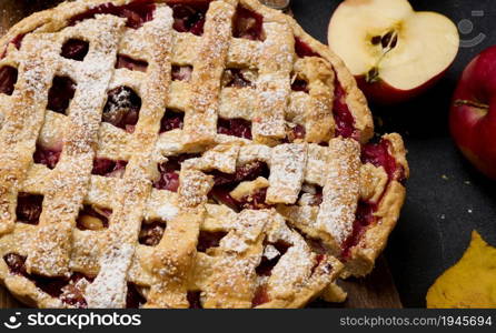 baked round traditional apple pie on brown wooden board and fresh red apples, top view