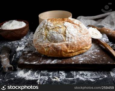 baked round white wheat bread on a brown wooden board and ingredients